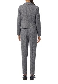 Tailored suit set in a textured gray and blue fabric, featuring a fitted blazer and slim-fit trousers. Shoes are black with a low heel.