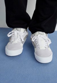 Graue und weiße Low-Top Sneaker mit Wildleder- und Lederpanelen, runder Zehenpartie, weißen Schnürsenkeln und einer Gummisohle.