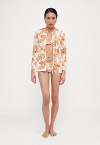 White swimwear set featuring orange floral patterns, including a long-sleeve zip-up top and matching bikini brief, made from lightweight material.