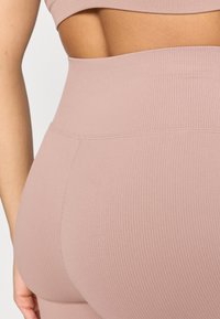 Ροζ φωτεινό ριμπ κολάν με ψηλή μέση, διαθέτει αδιάκοπο σχεδιασμό και απαλό ύφασμα, με διακριτικές ραφές κατά μήκος της μέσης.