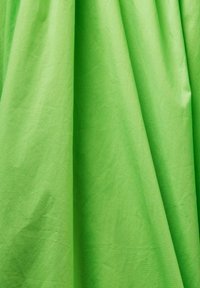 Tissu vert brillant avec des plis doux et une texture subtile, suspendu verticalement et se chevauchant en drapés délicats.