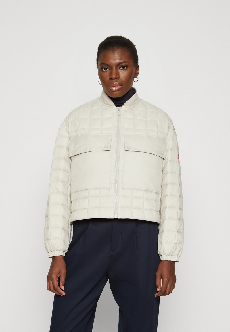 Quilted lettvekts puffer-jakke i lys beige med elastiske mansjetter, glidelås foran og to brystlommer. Minimalistisk design og cropped lengde.