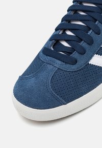 Mörkblå sneaker i mocka med perforerad yta, vit gummisula och matchande snören, med en enkel design.