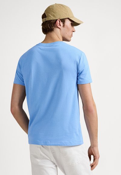 Φωτεινό γαλάζιο βαμβακερό μπλουζάκι με κοντά μανίκια και στρογγυλή λαιμόκοψη, από πίσω όψη. Το ύφασμα φαίνεται λείο και χωρίς υφή.