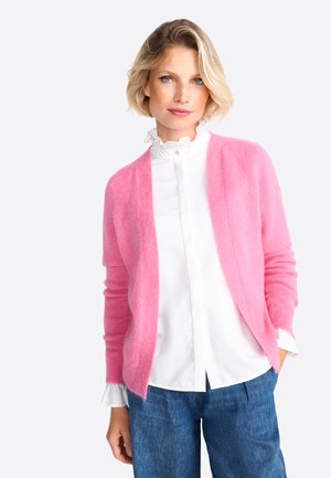 Pink, lightweight cardigan with open front, long sleeves, soft texture, layered over a white ruffled blouse and paired with blue denim.