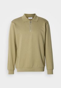 Kámzsás, hosszúujjú, cipzáras nyakú pólóing, puha szövetből készült, klasszikus gallérral és bordás mandzsettával.