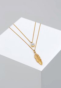 Goldene Lagenkette mit einem runden Kristallanhänger und einem detaillierten Federanhänger, beide an dünnen, zarten Ketten.