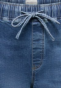 Pantalon en denim bleu avec une taille élastique et un cordon en denim assorti noué en nœud papillon au centre devant.
