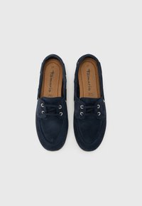 Tummansininen mokkanahkainen loafers-malli, jossa on nauhakiinnitys, ommelkorostukset ja teksturoitu pohjallinen. Koko 37 painettuna kengän sisälle.