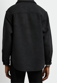 Svart skjortjacka i ullblandning med krage, lång ärm och rundad fåll. Tyget har en texturerad yta.