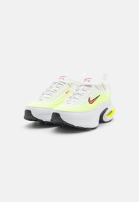 Nike-sneakers med vit överdel, gula accenter och svart sula, mesh-material, framträdande Air-enhet och röda logodetaljer.