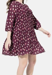 Plissiertes Kleid in tiefburgunderrot mit floralem Muster. Verfügt über lange, gepuffte Ärmel und einen ausgestellten Saum, hergestellt aus leichtem Stoff.