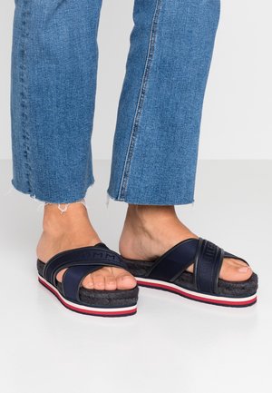 Granatowe klapki na płaskiej podeszwie z teksturowanymi paskami, wyposażone w grubą plecioną podeszwę oraz czerwono-biały pasek na spodzie.