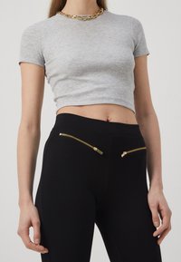 Harmaa ribattu crop-top ja mustat legginsit, joissa on kultaiset vetoketjupussit. Topissa on lyhyet hihat, kun taas legginsit ovat sileät ja joustavat.