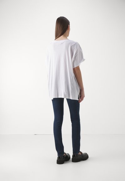 Fehér, pamut, nagyméretű póló rövid ujjakkal, oldalsó hasítékokkal, sötétkék skinny farmernadrággal és fekete, vastag talpú cipővel párosítva.