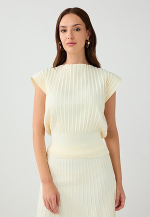Top plissettato color crema con maniche a cappuccio e vita a coste aderente. Realizzato in tessuto morbido, presenta righe verticali per texture.