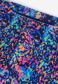 Tissu coloré à motifs présentant un mélange vibrant de bleu, orange, rose et vert sur un fond bleu marine foncé, avec une texture lisse et une finition douce.