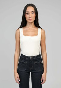 Débardeur côtelé beige clair à encolure carrée, associé à un jean noir taille haute avec des coutures contrastantes et des poches avant.