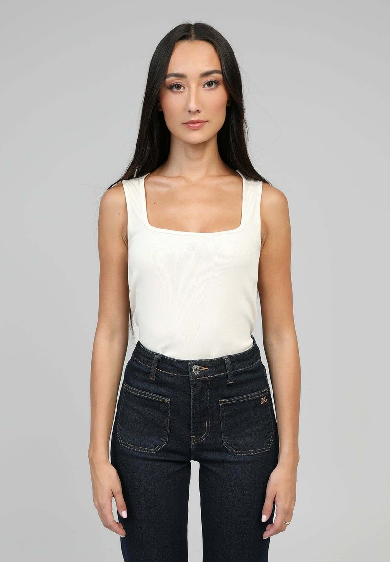 Débardeur côtelé beige clair à encolure carrée, associé à un jean noir taille haute avec des coutures contrastantes et des poches avant.