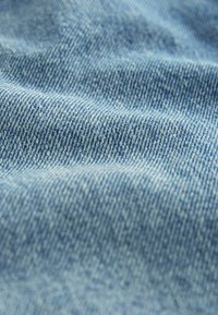 Gros plan sur un tissu en denim bleu clair montrant sa texture tissée et son motif sergé diagonal.