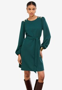 Tyrkysové šaty s dlhými nadýchanými rukávmi, zoštíhleným pásom a zlatými gombíkmi na pleciach. Hladká látka a dĺžka po kolená.