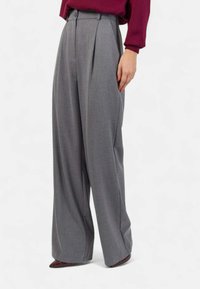 Pantaloni grigi a vita alta, plissettati, con tasche laterali e una vestibilità dritta, realizzati in un tessuto morbido, abbinati a una maglia bordeaux.