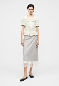 Ανοιχτοπράσινο μπλουζάκι με κοντά μανίκια και υφή, με εφαρμοστή μέση, σε συνδυασμό με γκρι φούστα με δαντελένιο τελείωμα και μαύρα επίπεδα παπούτσια.