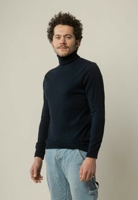 Navy coltrui gemaakt van een zacht materiaal, slim fit ontwerp, geribbelde manchetten en tailleband, gecombineerd met lichtblauwe denim jeans.