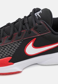 Sort atletiksko med rød og hvid Nike swoosh, rød syning, sorte snørebånd og hvid sål på lys baggrund.