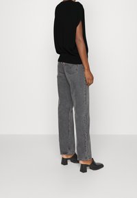 Černá blůza volného střihu s krátkým rukávem, spárovaná s šedými džíny s vysokým pasem a rovnými nohavicemi. Nošena s černými muly na podpatku.