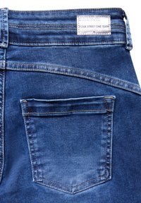 Dunkelblaue Jeans aus Denim mit einem klassischen Fünf-Taschen-Design, sichtbarem Nähen und einem Etikett am Bund. Glatter, mittelschwerer Textil.