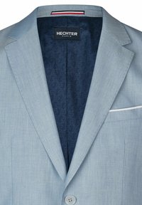 Helles blaues Blazer aus glattem Stoff, mit einem navy-blauen gemusterten Futter, einer einzelnen weißen Akzenttasche und einem Logotag am Kragen.