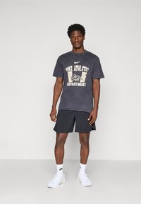 Tamsiai pilkos spalvos medvilnės marškinėliai su balta "Nike Athletic Department" logo, derinami su juodomis šortais ir baltais sportiniais batais.