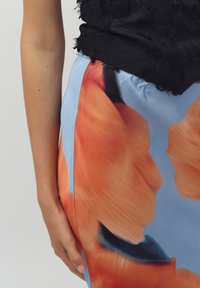 Kleurige bloemenrok met oranje en blauwe tinten, gemaakt van een zachte stof. Heeft een zijnaad en een contrasterend zwart gestructureerd top.