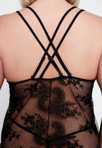 Zwarte kant lingerie met een bloemmotief, voorzien van crisscross rugbanden en verstelbare hardware. Doorzichtig materiaal benadrukt het ontwerp.