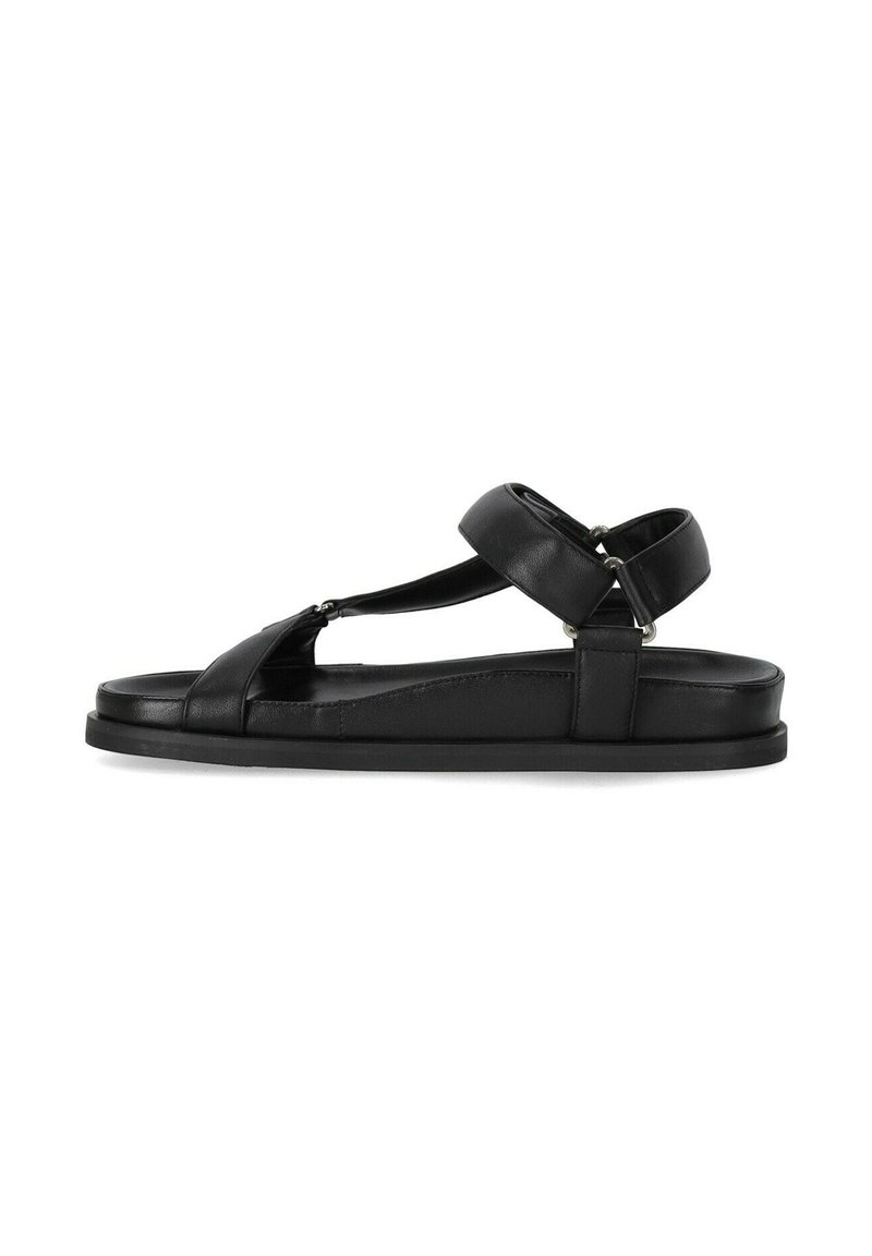 Sandalo in pelle nera con punta aperta, cinturini incrociati e cinturino alla caviglia sul retro. Caratterizzato da una suola piatta e un design minimalista.