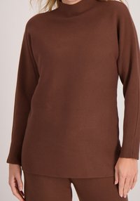 Bruine gebreide trui met een hoge hals en geribde boorden, met een gladde textuur en een losse pasvorm.