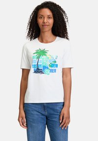 T-shirt blanc à manches courtes avec un motif de palmier coloré et des graphiques textuels dans des tons de bleu et de vert, assorti à un jean bleu.