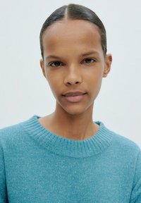 Blauer Wollpullover mit geripptem Rundhalsausschnitt, glatter Textur und körpernahem Design. Der Hintergrund ist neutral und minimalistisch.