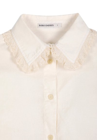 Chemise crème boutonnée avec col pointu et délicate bordure en dentelle le long des bords du col, étiquetée Bobo Choses.