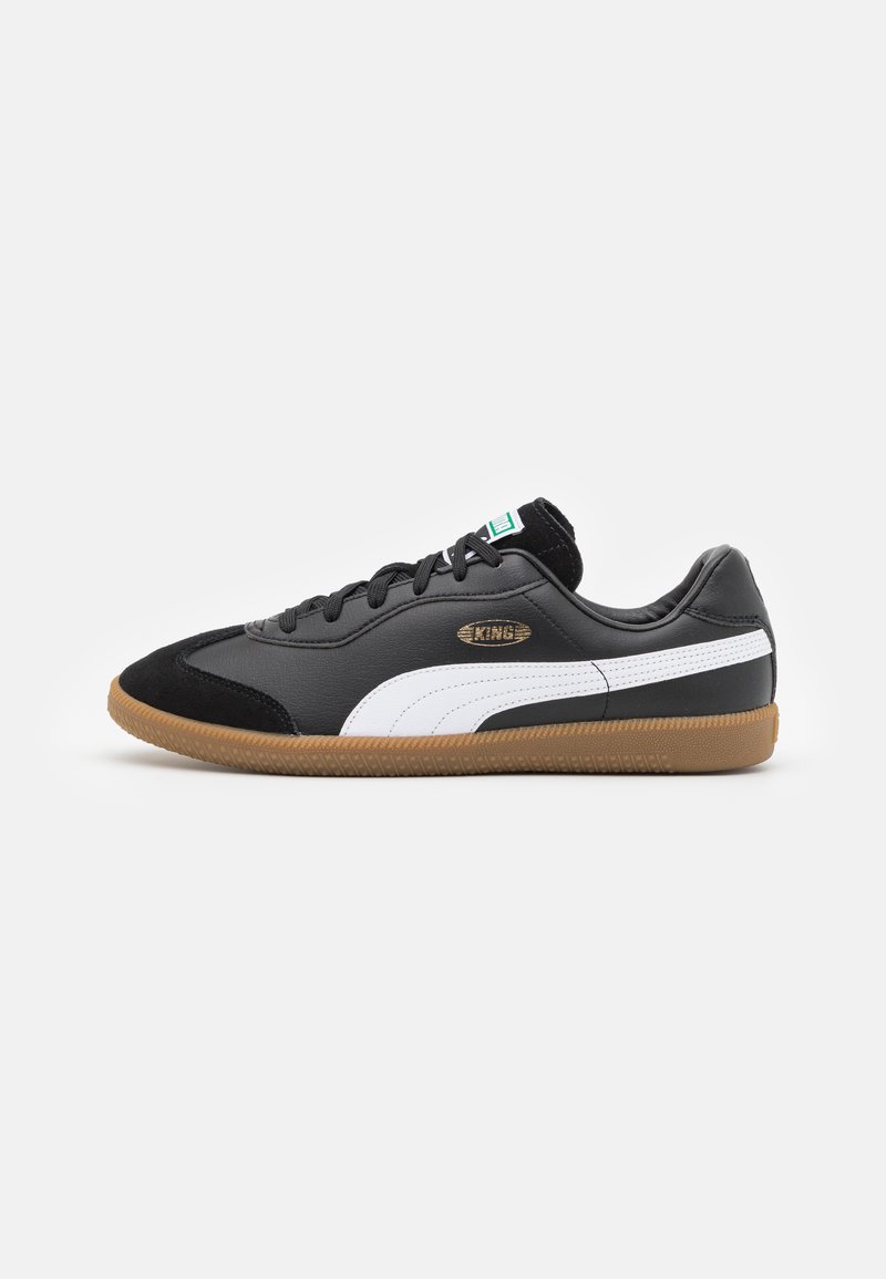 Sneaker in pelle nera con striscia bianca, suola in gomma color gomma e dettagli in suede nera. Presenta lacci e un logo dorato sul lato.