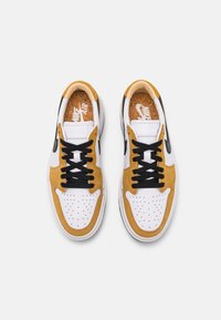 Nike Air tenisky s bílým koženým svrškem, žlutými semišovými detaily, černými šňůrkami, perforovanou špičkou a korkovou vložkou.