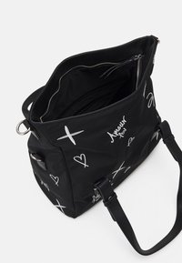 Schwarze Tasche aus Nylon mit weißen handgeschriebenen Akzenten, ausgestattet mit einem Reißverschluss, geräumigem Innenraum und zwei schwarzen Schulterriemen.