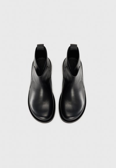 Botas de tobillo de cuero negro con un acabado suave, paneles laterales elásticos y tiradores para ponerlas con facilidad. Punta redondeada y diseño minimalista.