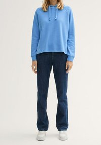 Ljusblå hoodie med kenguruficka, ribbade ärmslut, kombinerad med mörkblå raka jeans och vita sneakers. Avslappnad outfit.