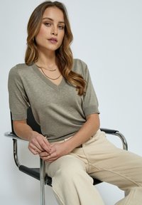 Top a manica corta con scollo a V in tessuto jersey grigio chiaro, caratterizzato da una silhouette aderente e dettagli a coste, abbinato a pantaloni beige a gamba larga.