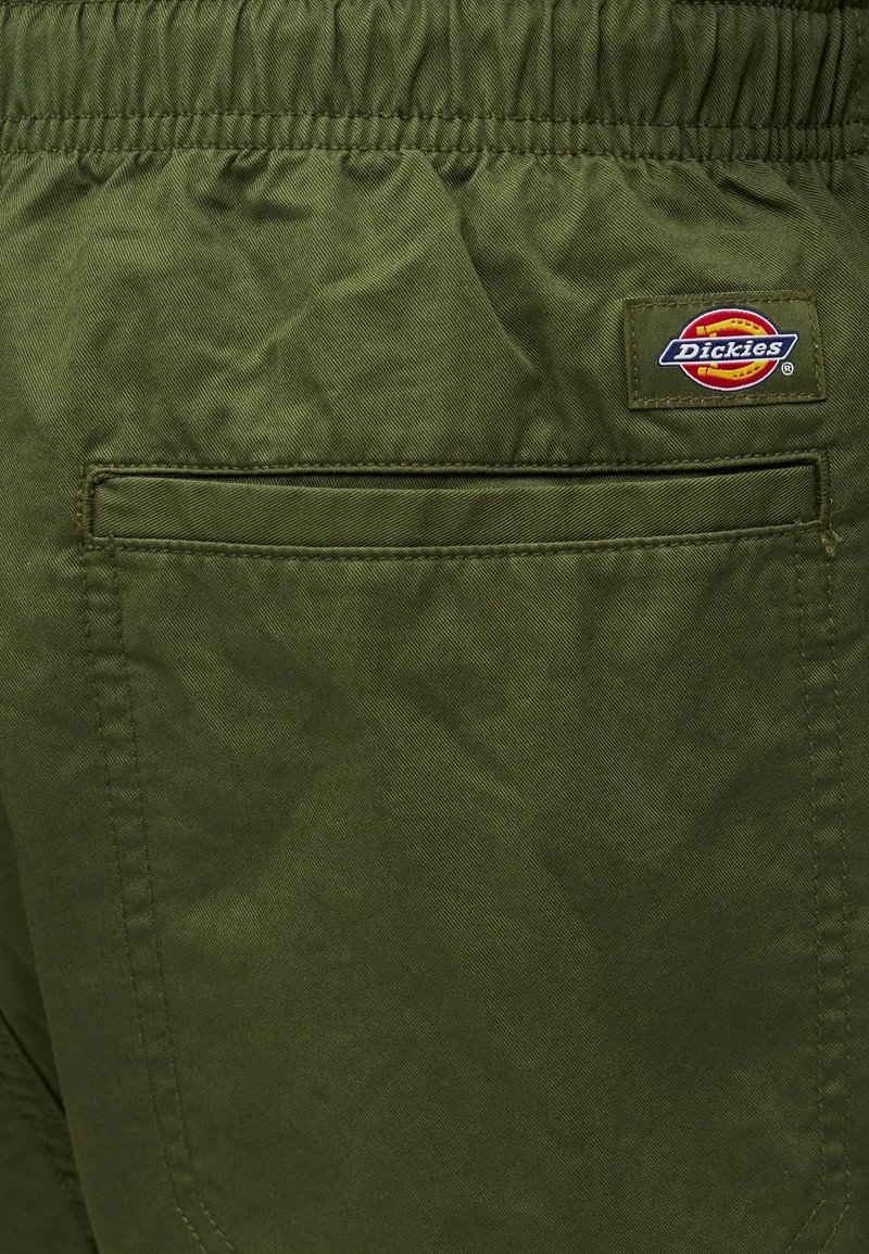 Gesäßtasche einer olivgrünen Hose mit elastischem Bund und einem rechteckigen Dickies-Markenlogo oberhalb der Tasche.