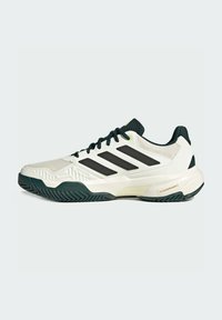 Sneaker de sport blanc avec des rayures noires, tige texturée, accents verts et semelle en caoutchouc présentant un motif en chevrons.