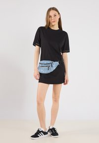 Rochie scurtă neagră cu mâneci scurte și detalii din dantelă, asociată cu o borsetă albastră cu paiete, care are două buzunare cu fermoar și accesorii negre.