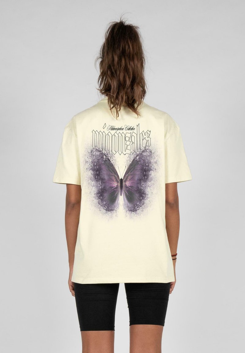 Camiseta de color amarillo claro con un gran gráfico de una mariposa morada en la parte posterior, acompañado de texto negro en la parte superior. Mangas cortas y corte relajado.